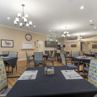 A spacious dining area with neatly arranged tables and chairs, well-lit by elegant chandeliers.