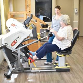An elderly woman is using a leg press machine with the guidance of a professional.