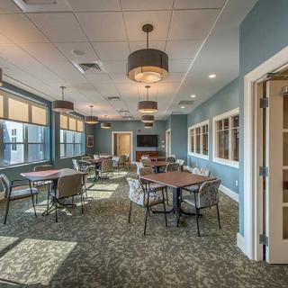 A spacious meeting room with tables, chairs, and large windows providing natural light.