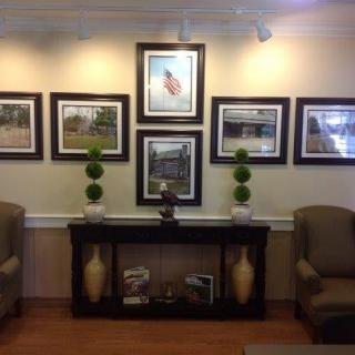 A waiting room interior featuring framed artwork, two chairs, and decorative plants.