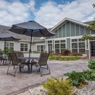 A spacious outdoor patio area with tables and umbrellas, surrounded by a residential house and garden.