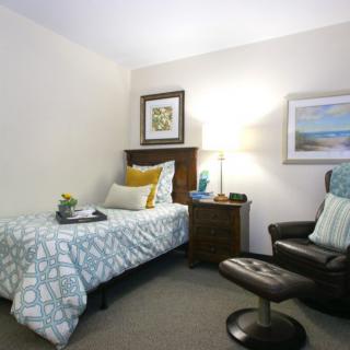 A cozy bedroom with a single bed and an armchair, featuring simple decor and soft lighting.