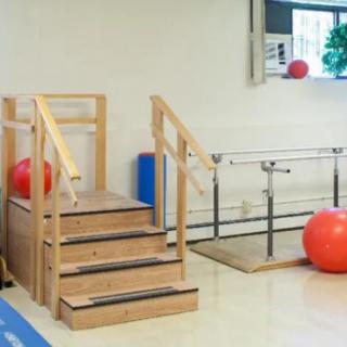 A physical therapy room equipped with stairs, parallel bars, and exercise balls for rehabilitation exercises.