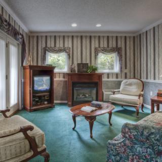 A traditional living room with vintage furniture, featuring a fireplace and striped wallpaper.