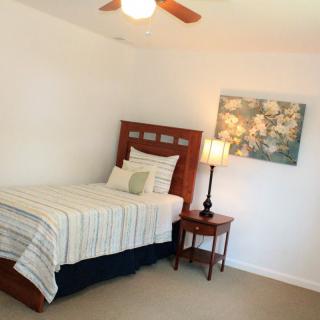 A minimalist bedroom featuring a single bed with striped bedding, a nightstand with a lamp, and a piece of artwork on the wall.