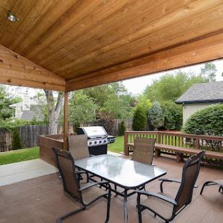 A cozy outdoor patio featuring a dining table, chairs, and a grill, surrounded by lush greenery.