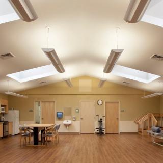 A spacious rehabilitation center room featuring skylights, wooden flooring, and various furniture pieces.