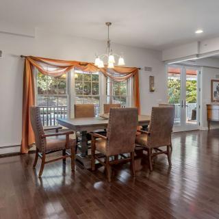 A spacious dining room with a wooden table, chairs, and a chandelier, featuring hardwood floors and large windows that allow in natural light.