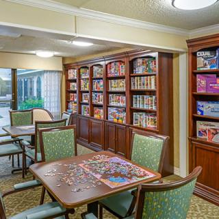 A cozy library with tables and chairs, featuring bookshelves filled with books and puzzles in progress.