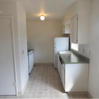 A compact kitchen with white walls, featuring a refrigerator and stove.