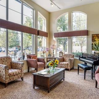 A cozy living room with comfortable seating, a piano, and large windows allowing ample natural light.