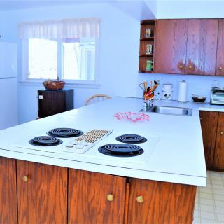 A spacious kitchen with a central countertop and built-in stove, surrounded by wooden cabinets.