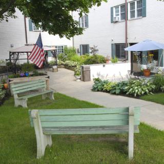 A tranquil garden with benches, a pathway, and vibrant plants outside a building displaying an American flag.