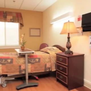 A well-lit hospital room with a bed, side table lamp, and mounted television.
