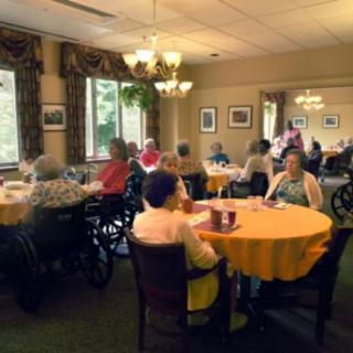 Elderly residents gather in a nursing home dining area, enjoying social time together.