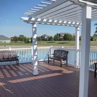 A waterfront deck with a white pergola and benches overlooking a lake.