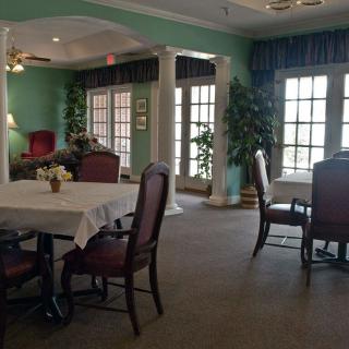 A cozy dining room with tables, chairs, large windows, and indoor plants.
