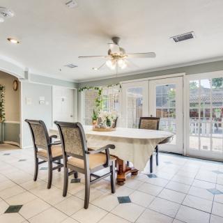 A bright dining room with a large table and wicker chairs, featuring a ceiling fan and ample natural light from the windows.