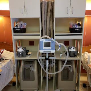 A bedside medical setup featuring monitoring equipment and supplies in a hospital room.