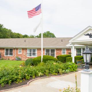 A brick building with an American flag flying overhead and a well-maintained garden in front.