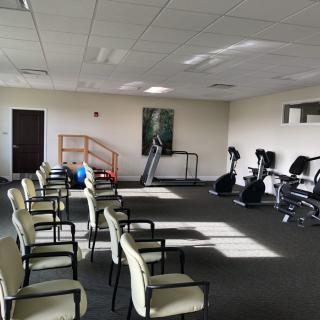 A well-lit gym with rows of chairs and various exercise equipment, including treadmills and stationary bikes.