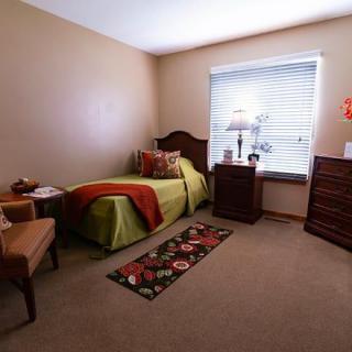 A cozy bedroom with a single bed, dresser, and chair near a window.