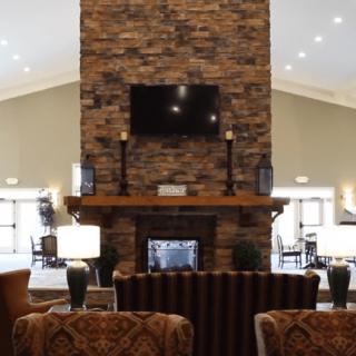 A modern lobby featuring a central brick fireplace with a mounted television and comfortable seating arrangements.