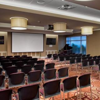 An empty conference room with rows of chairs facing a projector screen, set up for a meeting or presentation.