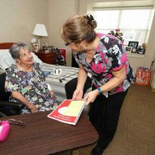 A caregiver is assisting an elderly woman in a nursing home setting.