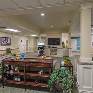 A spacious lobby area with a central table, potted plants, and a reception desk in the background.