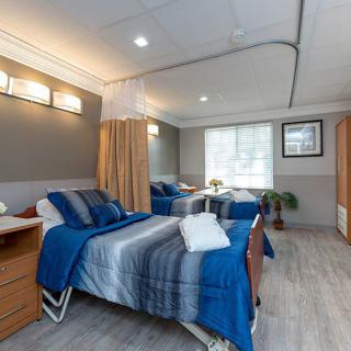 A modern hospital room with twin beds, blue bedding, and a dividing curtain.