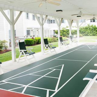 An outdoor shuffleboard court with seating under a covered area.