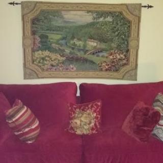 A cozy living room setup featuring a red couch adorned with decorative pillows and a beautiful tapestry hanging above.