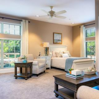 A modern bedroom with large windows, neutral tones, and comfortable furnishings.
