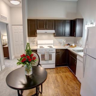 A modern kitchen in an apartment with dark cabinetry, a white stove and refrigerator, and a small dining table with red roses.