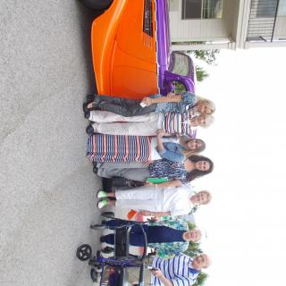 A group of people stand beside a brightly colored classic car in a residential area.