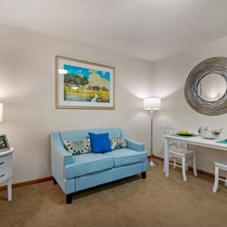 A cozy living room featuring a blue sofa, wall artwork, and a dining area with elegant decor.