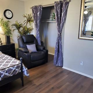 A cozy bedroom featuring a recliner chair, wooden flooring, and decorative plants.