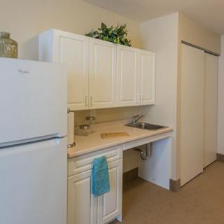 A small kitchen area with white cabinets, a refrigerator, and a countertop featuring a sink and towel.