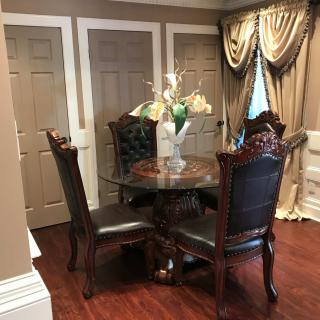 Elegant dining area with a round table, upholstered chairs, and decorative curtains.