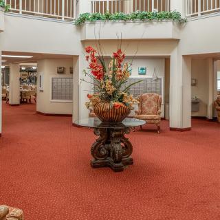 A spacious lobby area with red carpeting, featuring a central decorative table with an elaborate floral arrangement.