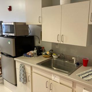 A small kitchen area with a fridge, microwave, sink, and white cabinets.