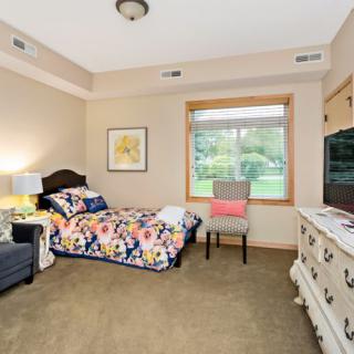 A cozy bedroom featuring a single bed with floral bedding, a window with a view, and neutral-toned decor.