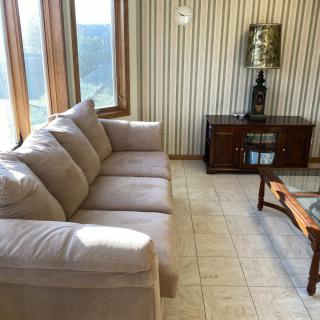A cozy living room with a beige sofa, glass coffee table, and large windows bringing in natural light.