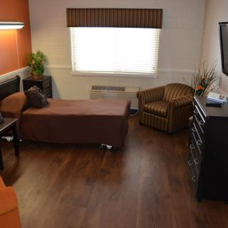 A cozy bedroom with a single bed, armchair, television, and dresser on wood flooring.