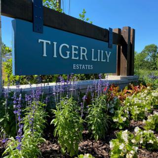 Entrance sign for Tiger Lily Estates surrounded by vibrant flowers and greenery.
