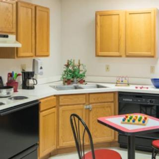 A cozy kitchen with wooden cabinets, a countertop with appliances, and a small table set with a chessboard.