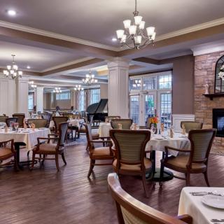 An elegant restaurant dining area with neatly arranged tables, classic chandeliers, and a grand piano.