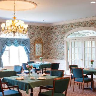 An elegant dining room with floral wallpaper, adorned with tables and chairs under a chandelier.