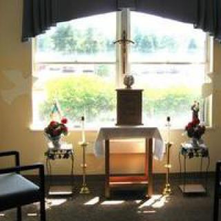A small chapel with an altar, featuring candles and flowers by a window.